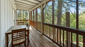 A covered porch with wooden railings and a table with chairs, overlooking a forested area. - 5 Mi to Lake Arrowhead Village: Cabin w/ Game Room (Lake Arrowhead)