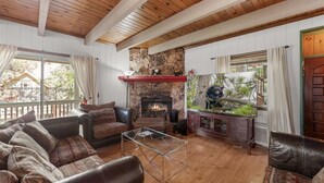 A cozy living room with a fireplace, leather sofas, and a glass coffee table. - 5 Mi to Lake Arrowhead Village: Cabin w/ Game Room (Lake Arrowhead)