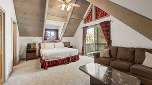 A bedroom with a bed, a brown leather sofa, a ceiling fan, and large windows with curtains. - 5 Mi to Lake Arrowhead Village: Cabin w/ Game Room (Lake Arrowhead)