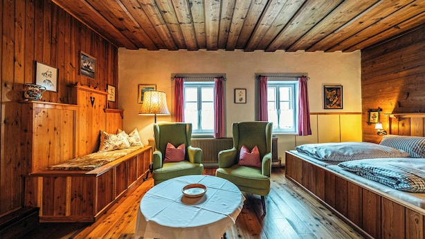 Ein Zimmer mit Holzboden, einem Bett, zwei Sesseln, einem Tisch und einer Bank.