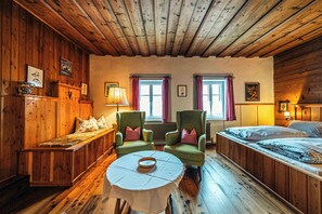 Ein Zimmer mit Holzboden, einem Bett, zwei Sesseln, einem Tisch und einer Bank.