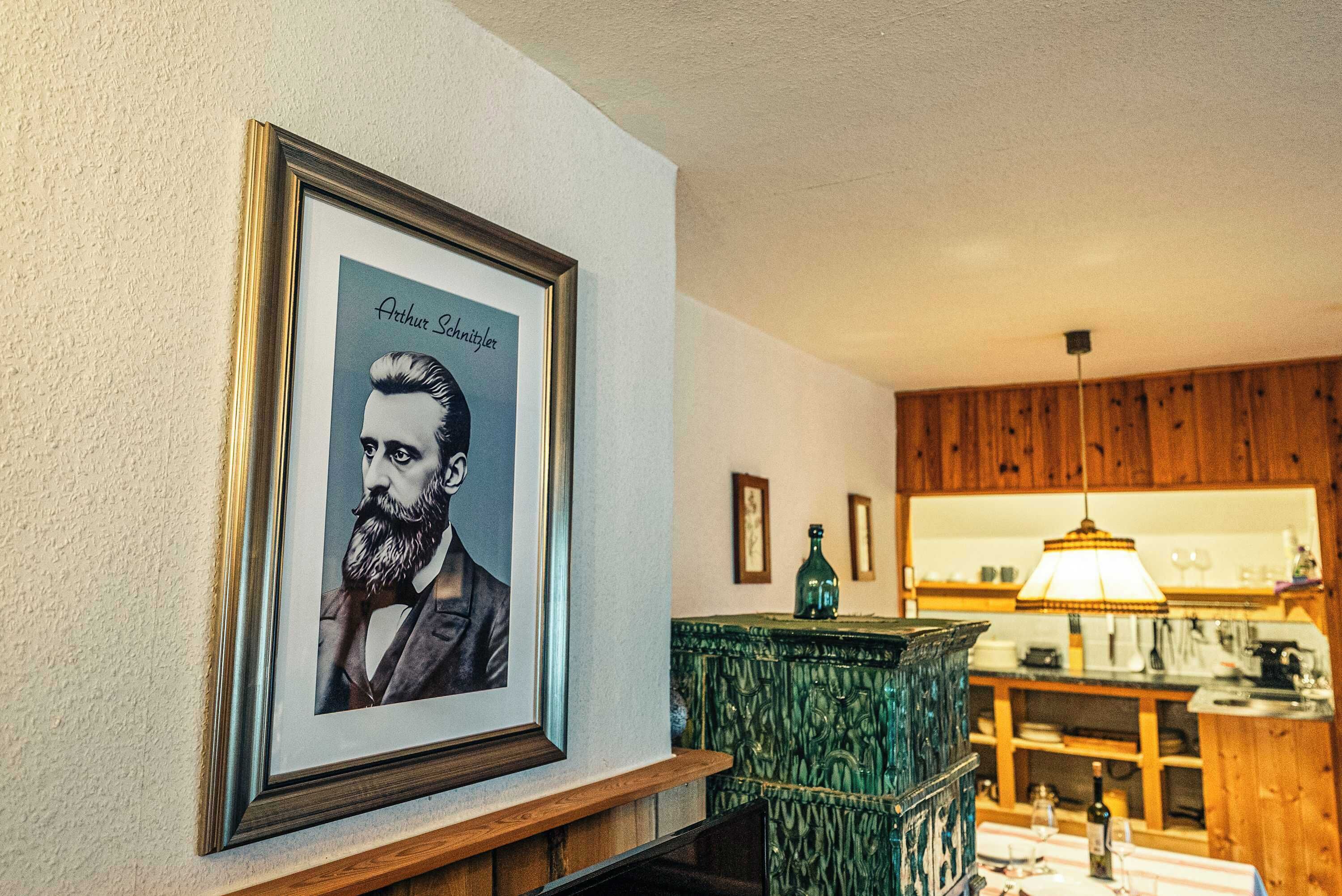 Ein gerahmtes Porträt an der Wand, ein Holzkabinent und ein Tisch mit einer Lampe.
