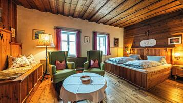 A cozy room with a wooden ceiling, a bed, two armchairs, a table with a bowl, and two windows with curtains.