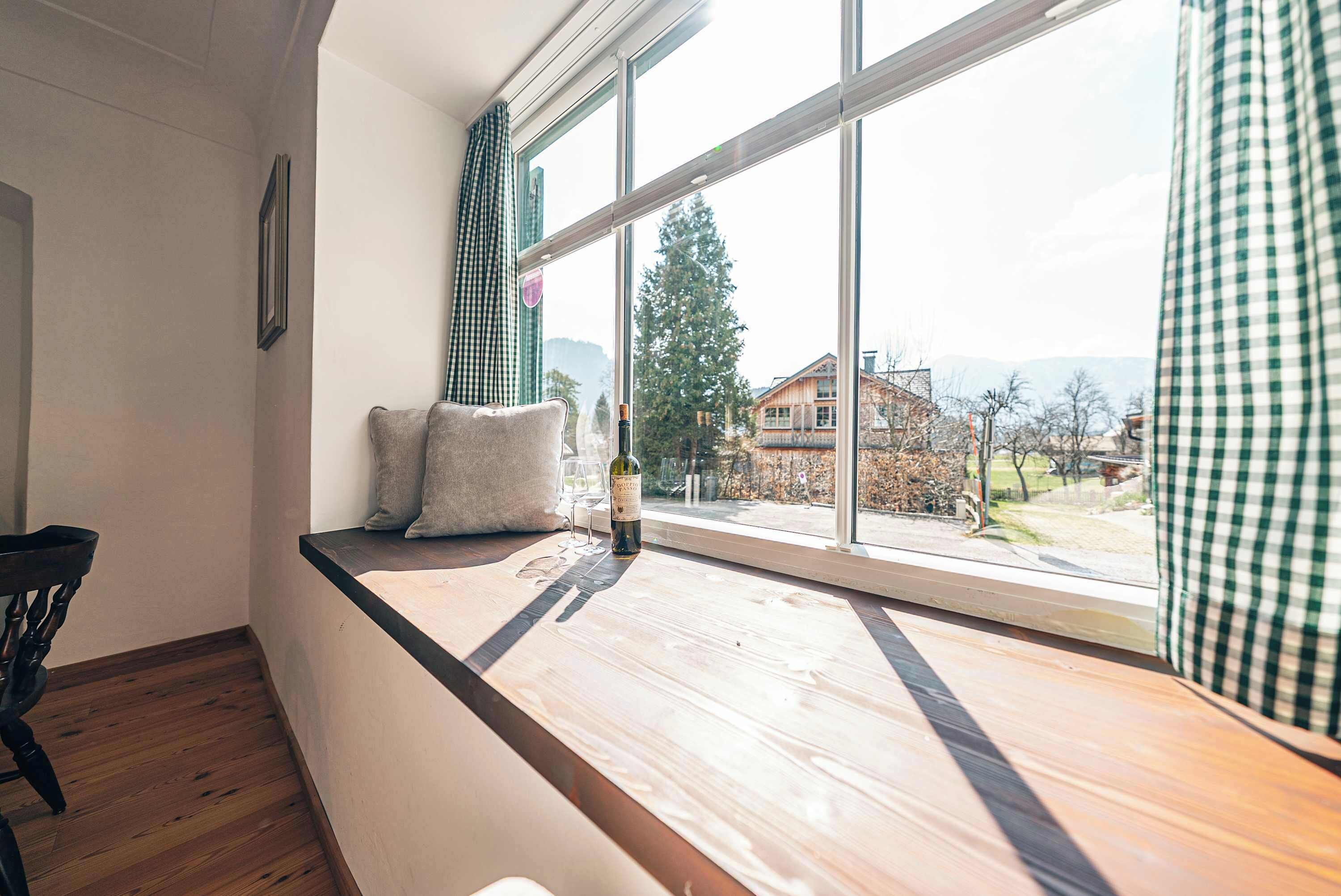 Ein Zimmer mit einem großen Fenster, einer hölzernen Bank, einem Stuhl und einer Weinflasche.