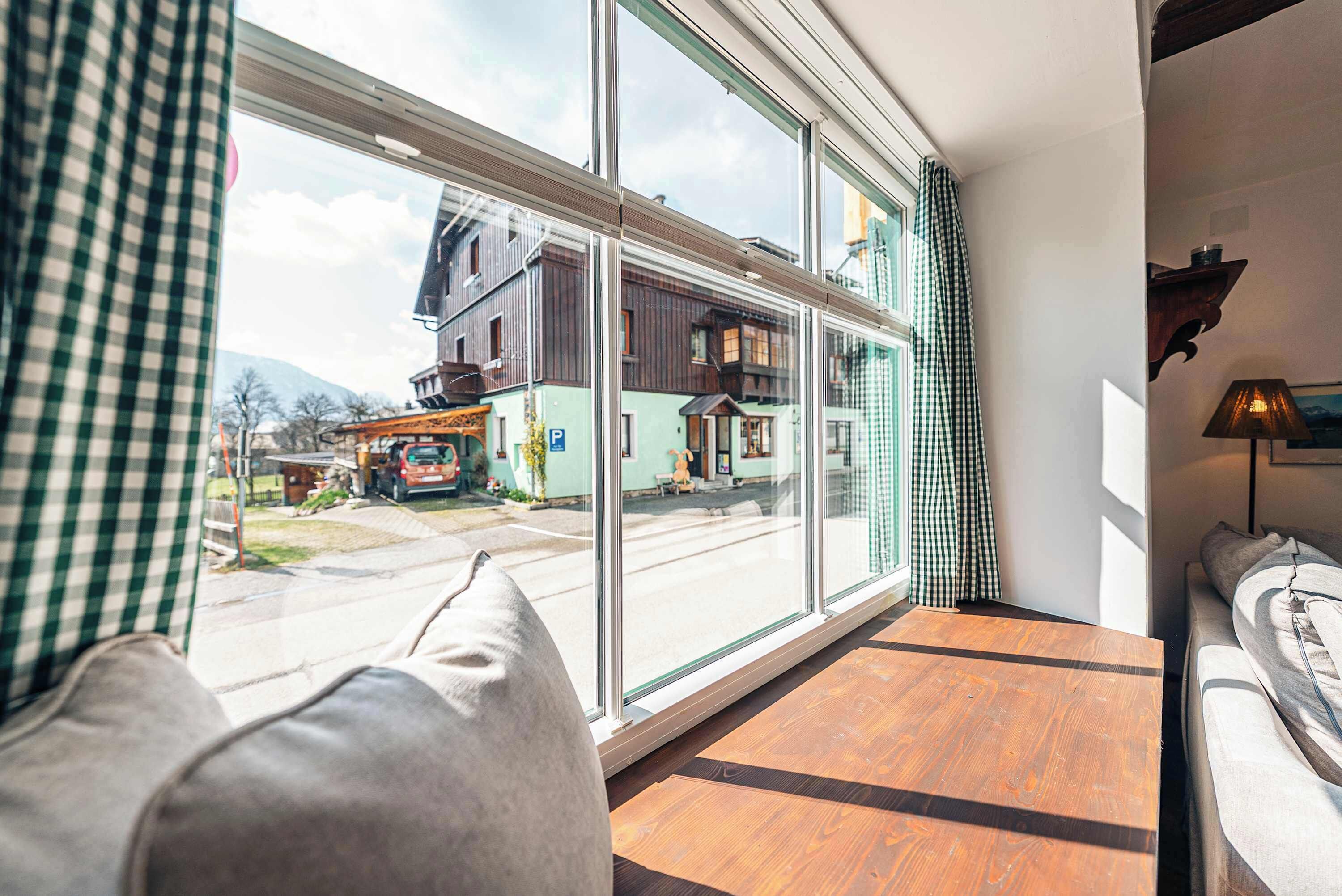 A room with a large window, a wooden floor, a sofa, and a lamp.