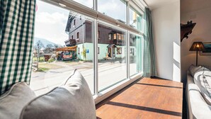 A room with a large window, a wooden floor, a sofa, and a lamp.