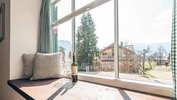 A room with a large window, a wooden bench, and a bottle of wine.
