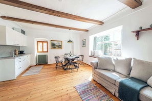 Eine moderne Küche mit Holzbalken, eine Essecke mit Tisch und Stühlen, ein Sofa und ein Fenster mit Blick.