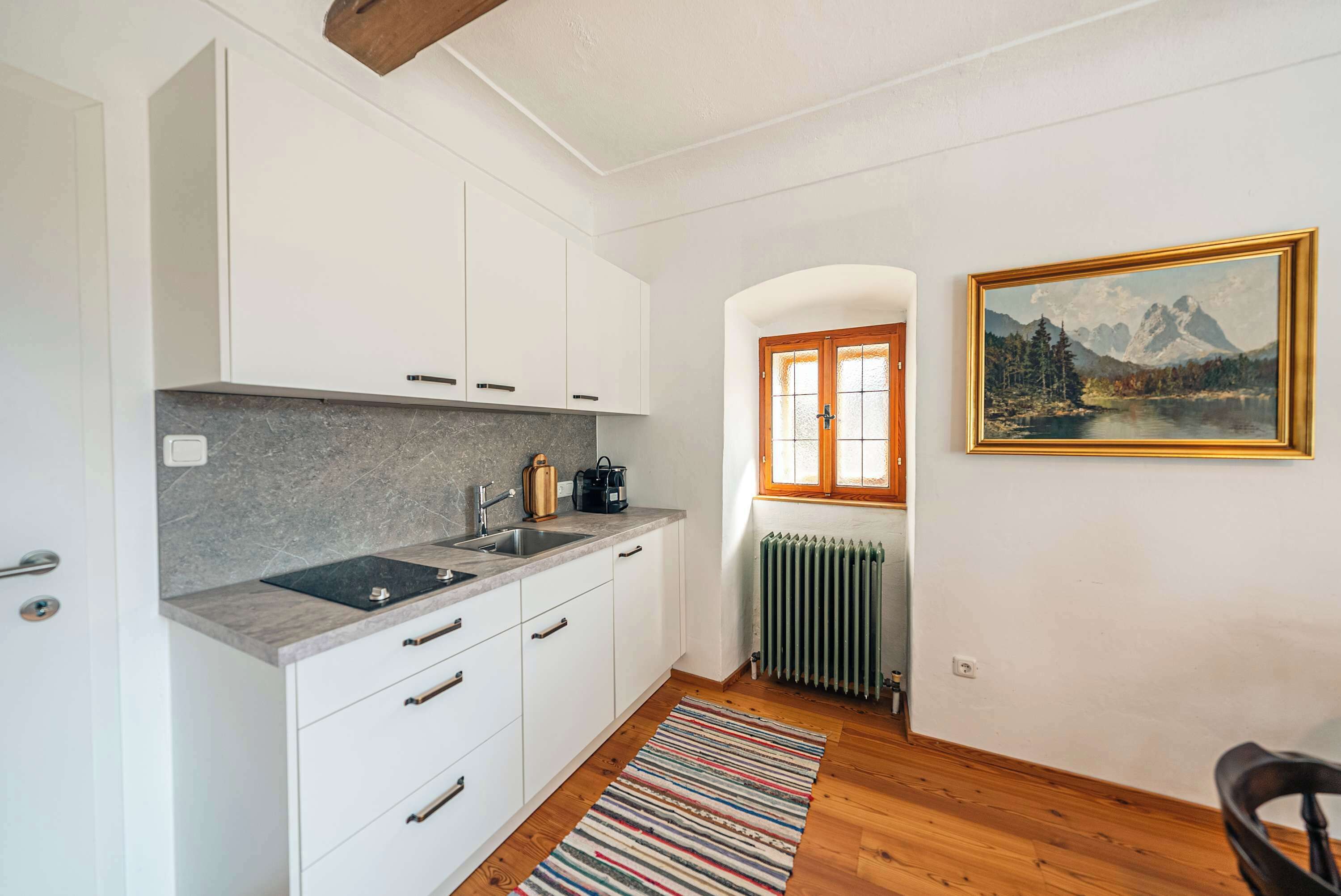 Une cuisine moderne avec des meubles blancs, un plan de travail en granit, un évier et un radiateur.