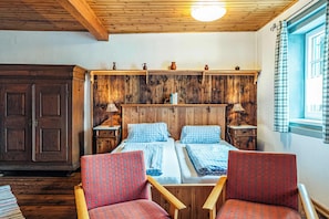 A room with two beds, wooden headboard, two nightstands, a wardrobe, and a window with curtains.