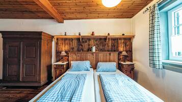 Ein Zimmer mit zwei Betten, einem Holzkopfende, einem Holzschrank und einem Fenster mit Vorhängen.