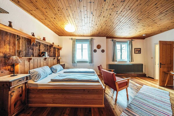 A wooden bedroom with a bed, a chair, a dresser, and two windows with curtains.