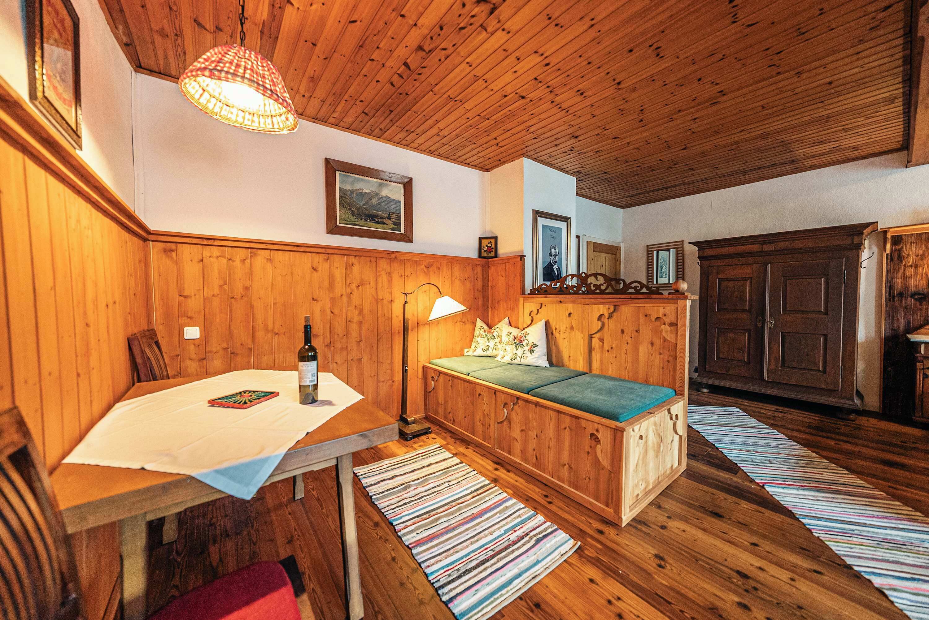 Ein Holzzimmer mit Tisch, Bank, Lampe und gerahmten Bildern an der Wand.