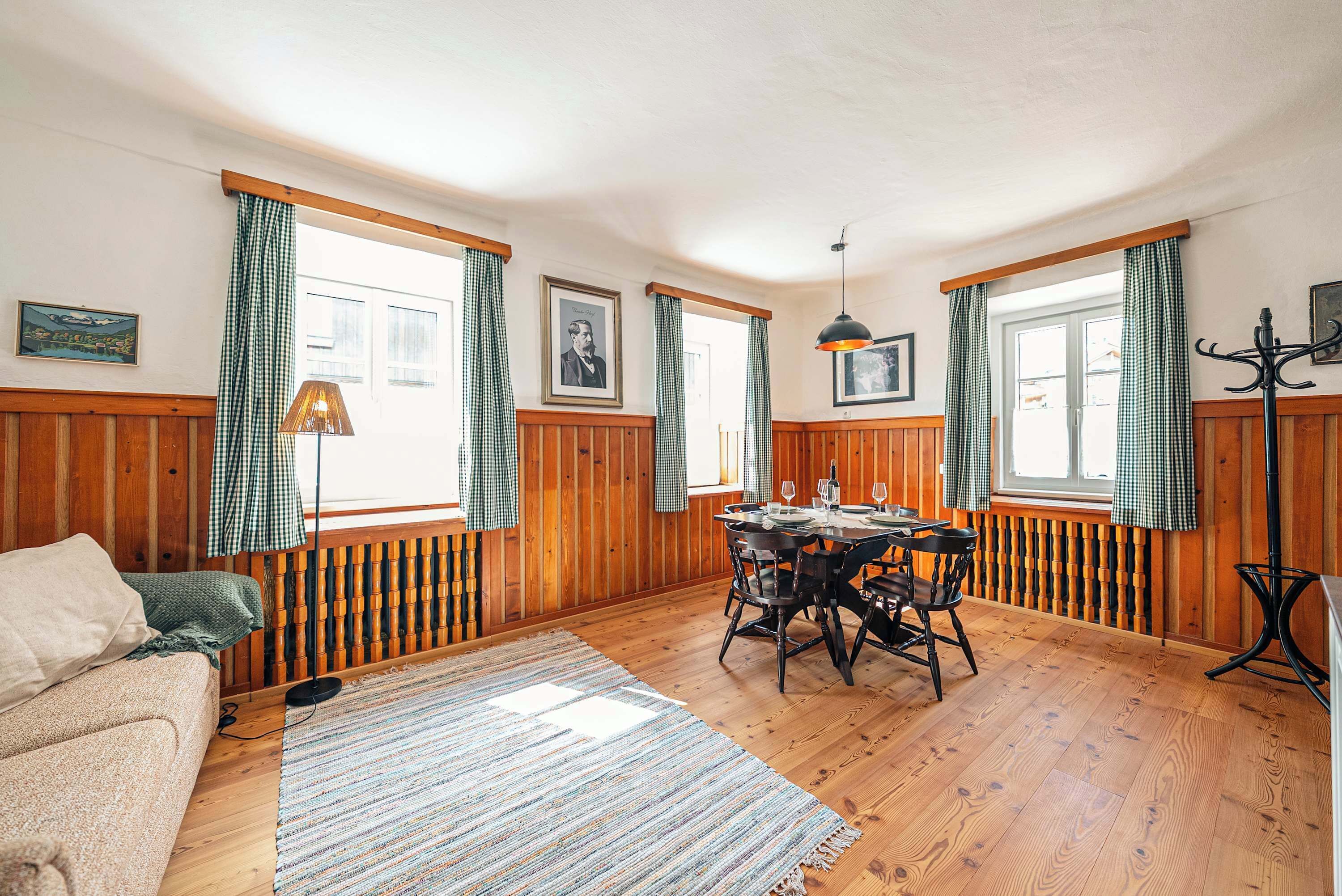 Ein Zimmer mit Holzwänden, einem Esstisch, Stühlen, einer Couch und einer Lampe.