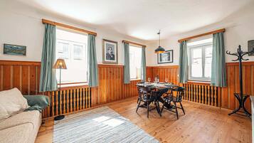 Ein Zimmer mit Holzwänden, einem Esstisch, Stühlen, einer Couch und einer Lampe.