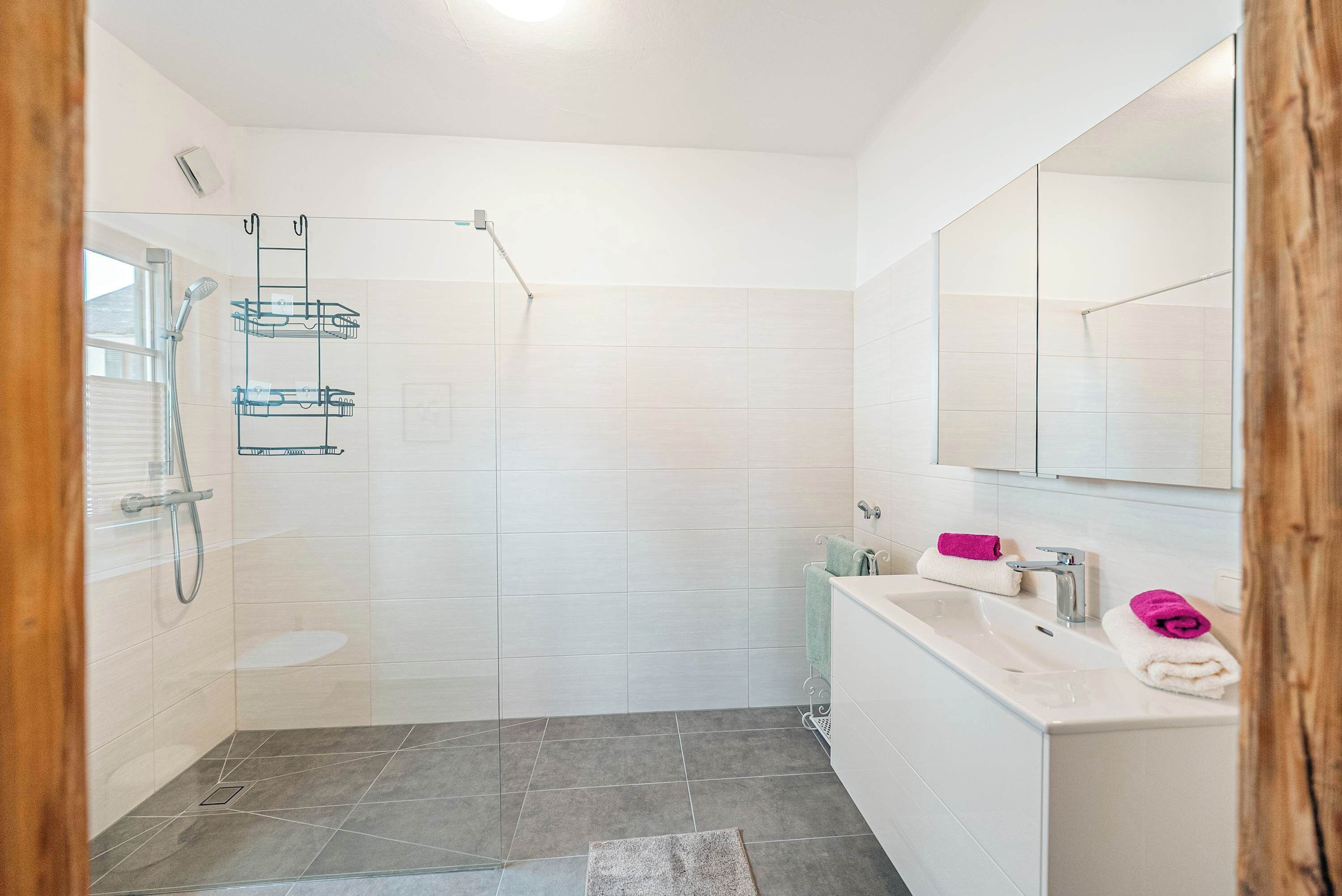 Un baño con cabina de ducha de vidrio, paredes de azulejos blancos, un lavabo blanco y un espejo.