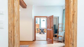 Un pasillo con piso de madera, una puerta que da a un comedor y una silla cerca de una ventana.