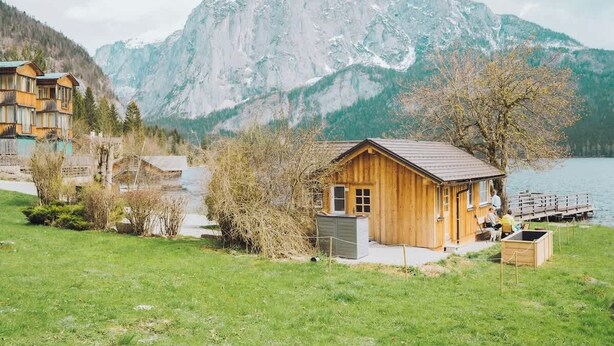 Una cabaña de madera con un muelle, rodeada de montañas y un lago.