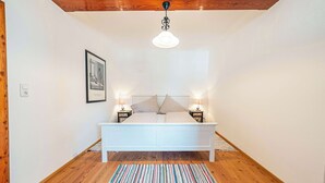Un dormitorio con cama blanca, alfombra a rayas, techo de madera y dos lámparas de noche.