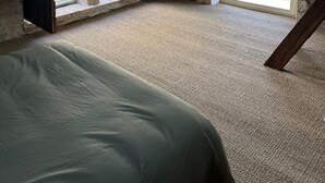 Ein rustikaler Raum mit schrägen Wänden, Steinwänden, einem Bett und großen, bogenförmigen Fenstern.