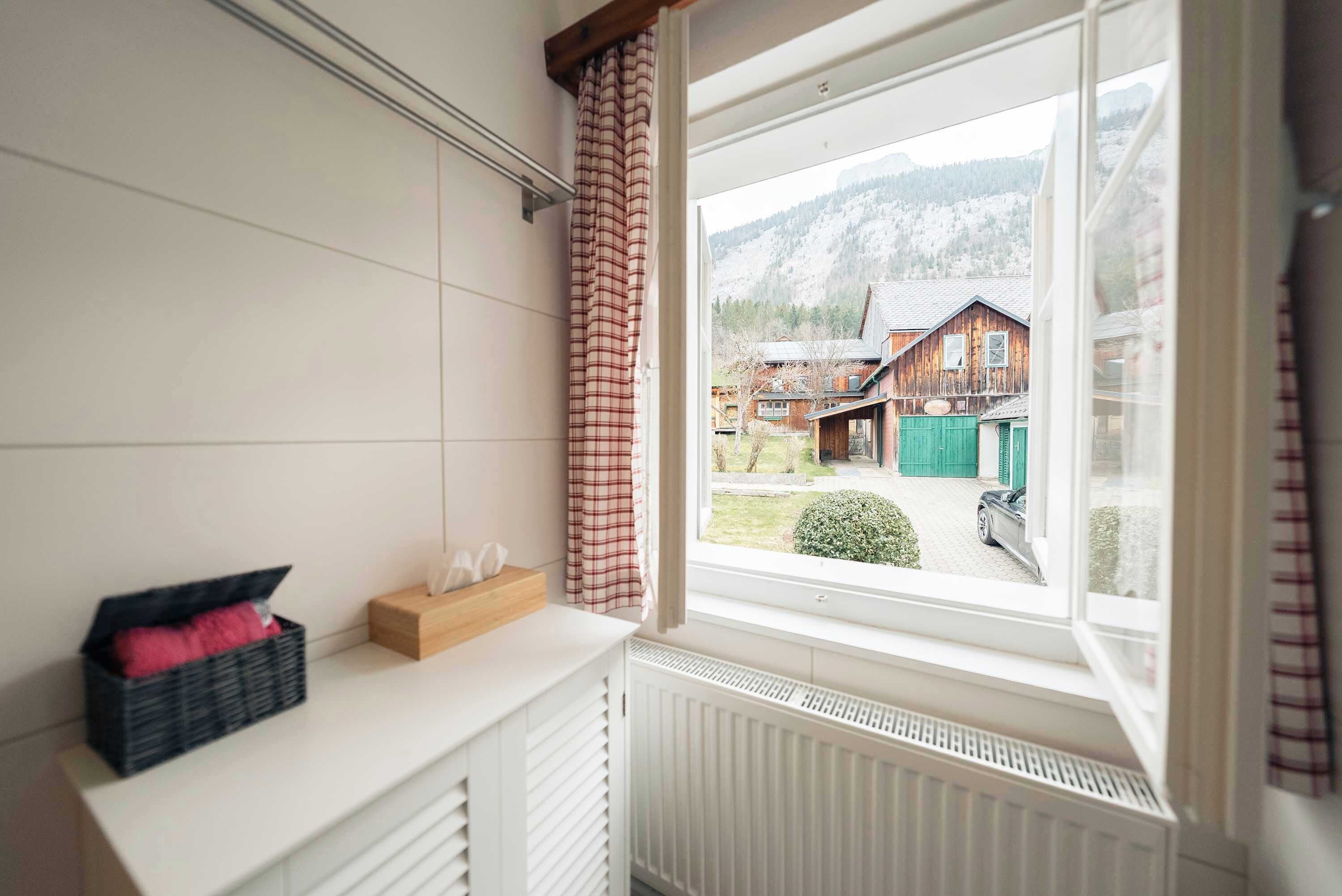 Et værelse med vindue, radiator, hvide vægge og udsigt til huse og bjerge.