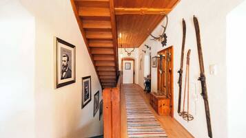 Eine Holztreppe führt zu einem Raum mit einem gerahmten Porträt, einem Streifen Teppich und an der Wand befestigten Ski.