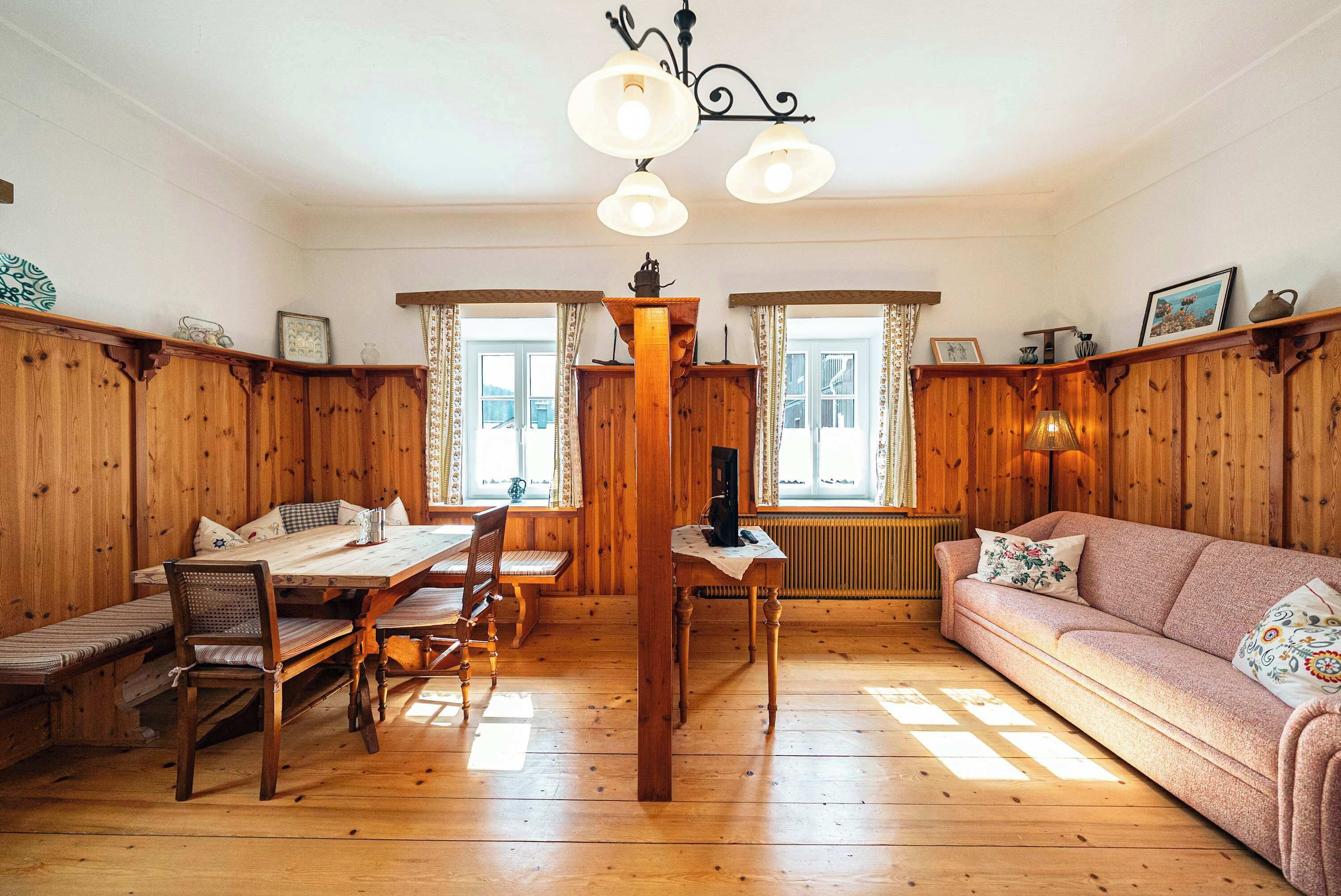 Ein Holzinterieur mit Esstisch, Stühlen, einer Couch und einer Chandelieber.