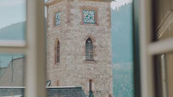 Ein Steinturm mit einer Uhr, einem steilen Dach und Blick auf eine bewaldete Bergkette.