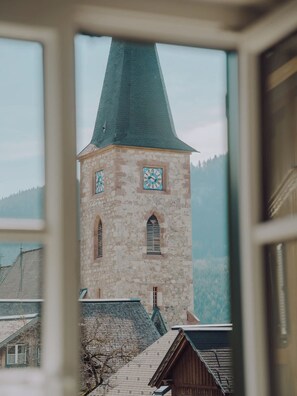 Ein Steinturm mit einer Uhr, einem steilen Dach und Blick auf eine bewaldete Bergkette.