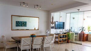 Een moderne woonkamer met een eetgedeelte, een grote spiegel, een flatscreen televisie en een schuifdeur naar een balkon.