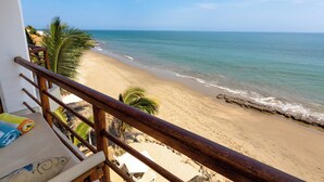 Uitzicht op een strand vanaf een balkon met houten leuning, een palmboom en een zandstrand.