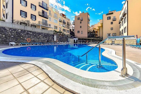 A swimming pool with a curved edge, surrounded by a stone wall and a metal railing.