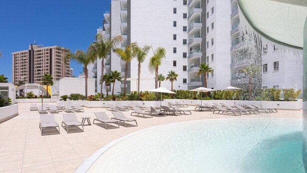 A poolside area with sun loungers and palm trees, surrounded by modern buildings. - Rental unit in Adeje · ★New · 2 bedrooms · 2 beds · 2 baths (Adeje)