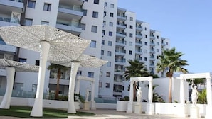A modern building with balconies, white umbrellas, and statues in a courtyard. - Rental unit in Adeje · ★New · 2 bedrooms · 2 beds · 2 baths (Adeje)