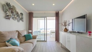 A modern living room with a sofa, a flat-screen TV, and a view to an outdoor balcony. - Rental unit in Adeje · ★New · 2 bedrooms · 2 beds · 2 baths (Adeje)