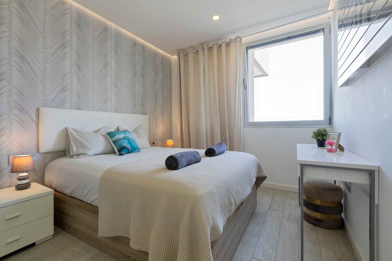 Un dormitorio moderno con una cama grande, una mesita de noche, un escritorio y una ventana con cortinas.