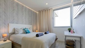 A modern bedroom with a large bed, a bedside table, a desk, and a window with curtains. - Rental unit in Adeje · ★New · 2 bedrooms · 2 beds · 2 baths (Adeje)