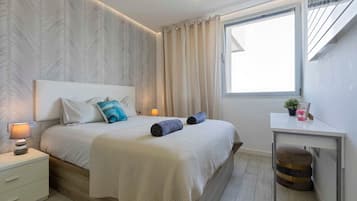 Un dormitorio moderno con una cama grande, una mesita de noche, un escritorio y una ventana con cortinas.