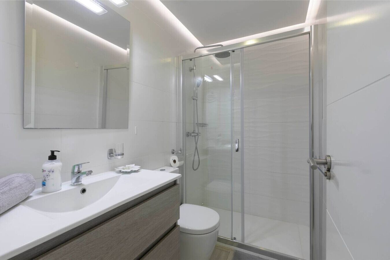 Une salle de bain moderne avec une douche à parois de verre, un grand miroir et un meuble-lavabo agrémenté d’une serviette.