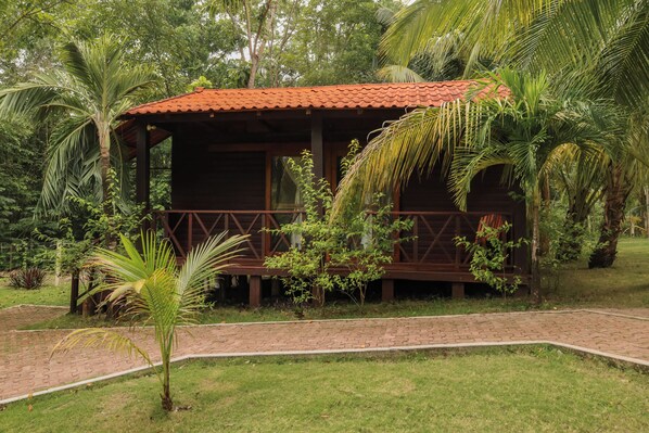 Una cabaña de madera con techo de tejas, rodeada de exuberante follaje y palmeras.