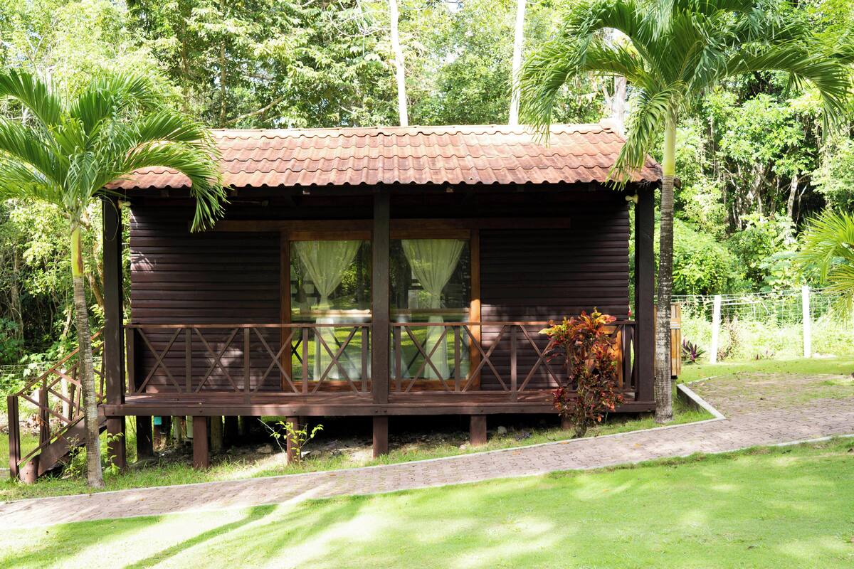 A wooden cabin with a balcony, surrounded by lush greenery.