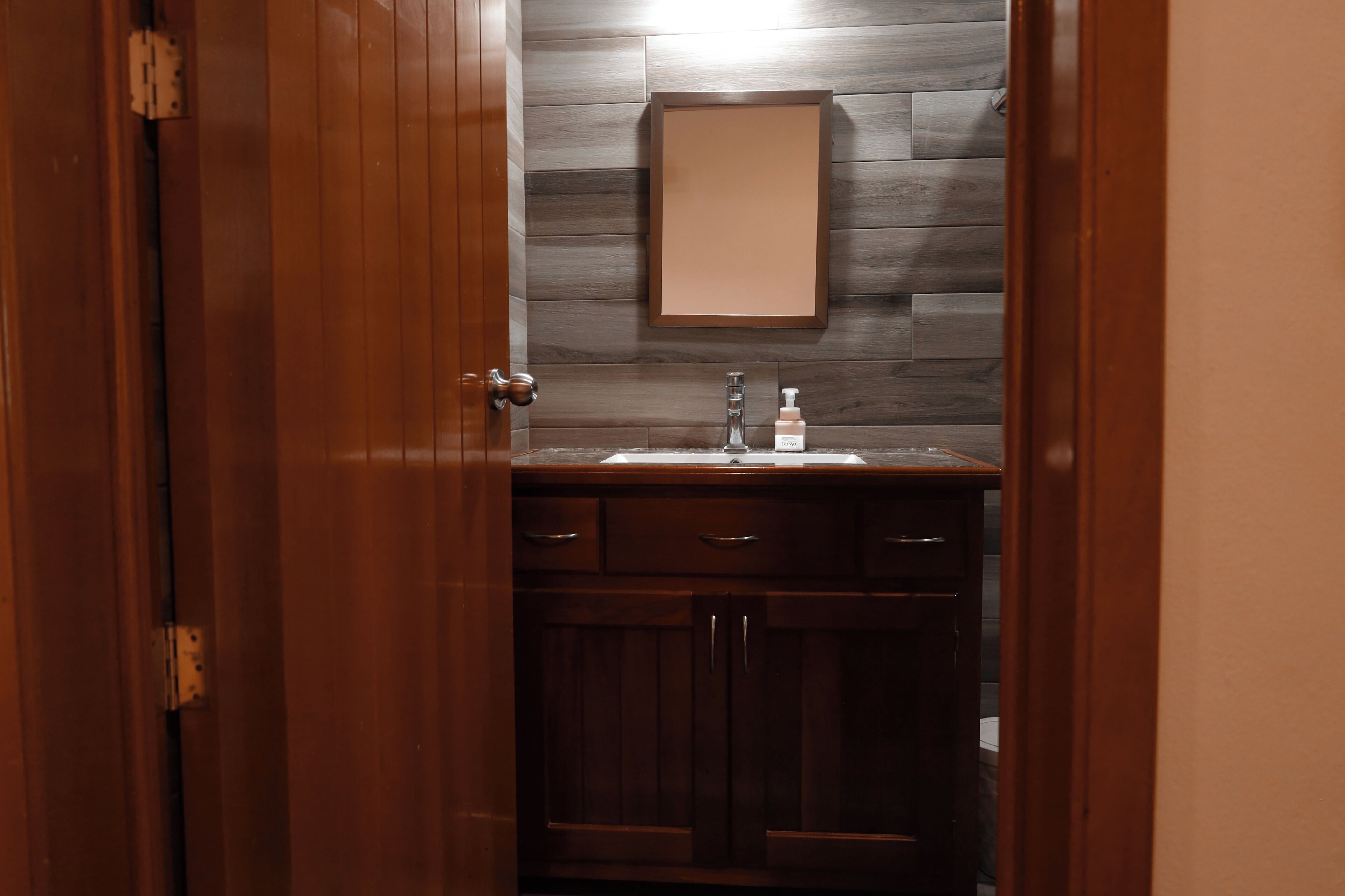 A bathroom with a wooden vanity, a mirror, and a sink.