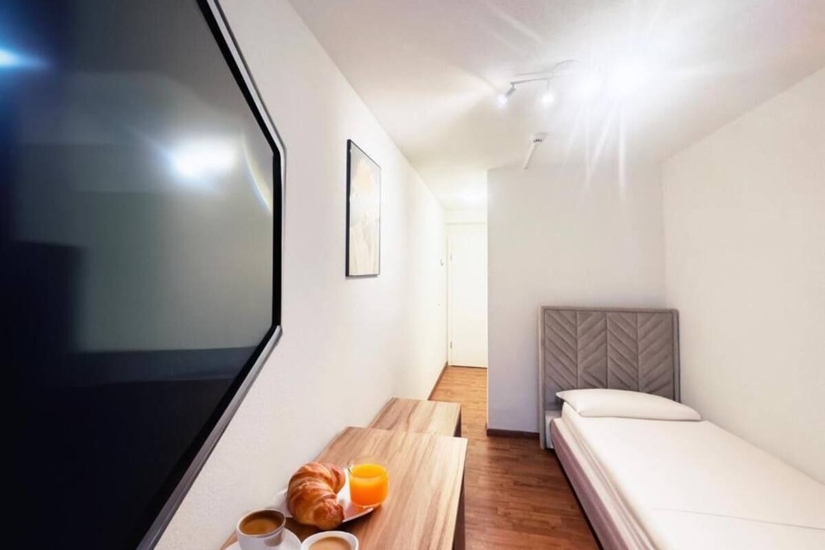 Een moderne hotelkamer met een bed, een klein tafeltje met ontbijt, een televisie en uitzicht op de gang.