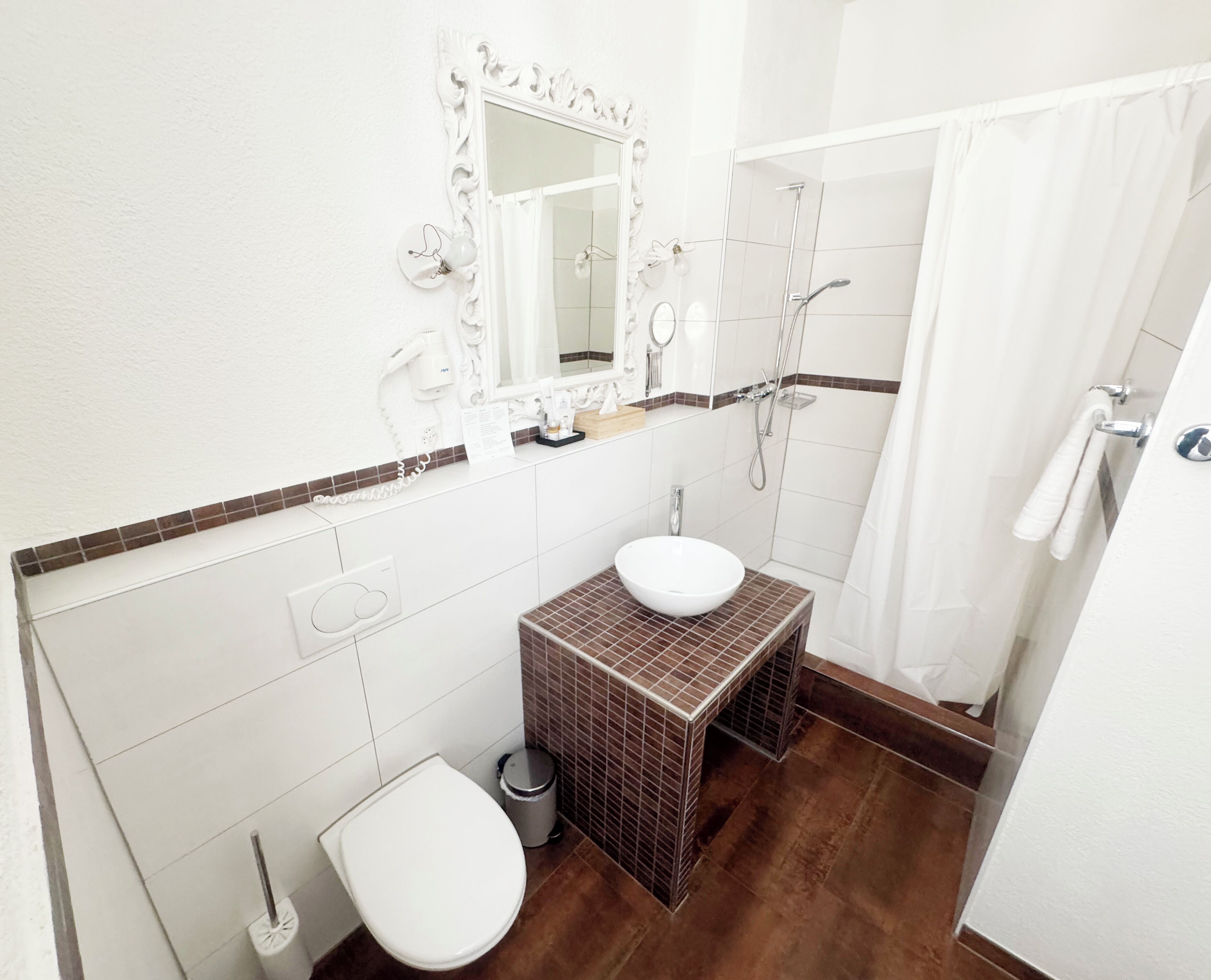 A bathroom with a white sink, a toilet, a shower, and a mirror with a decorative frame.