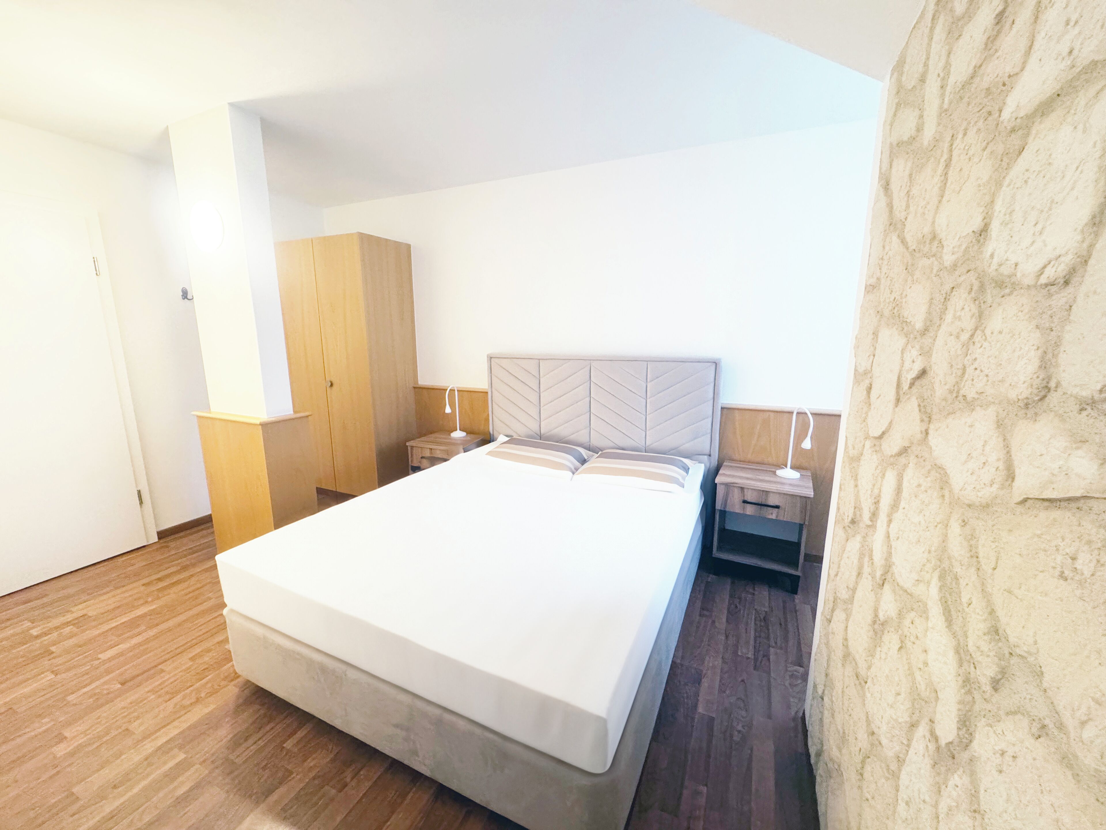 Un dormitorio con una cama grande, un armario de madera, mesitas de noche y una pared de piedra.