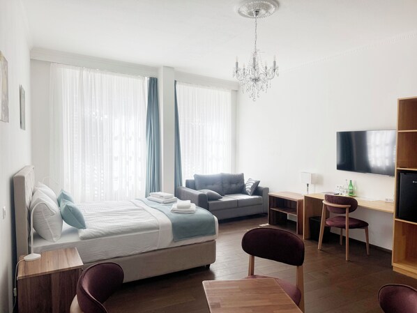 Una habitación de hotel moderna con una cama, un sofá, un escritorio, un televisor y una araña.