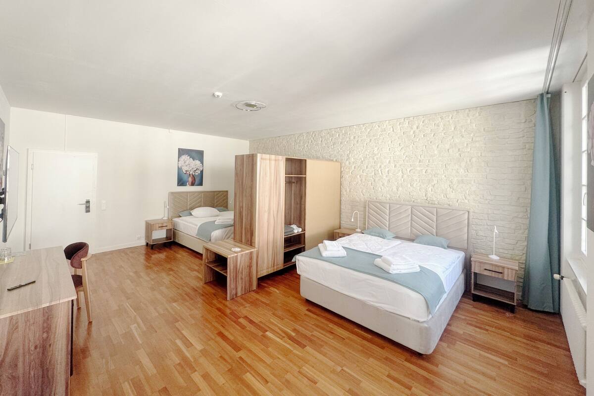 Een moderne slaapkamer met twee bedden, een houten garderobe, een bureau en een wand met een steenstructuur.