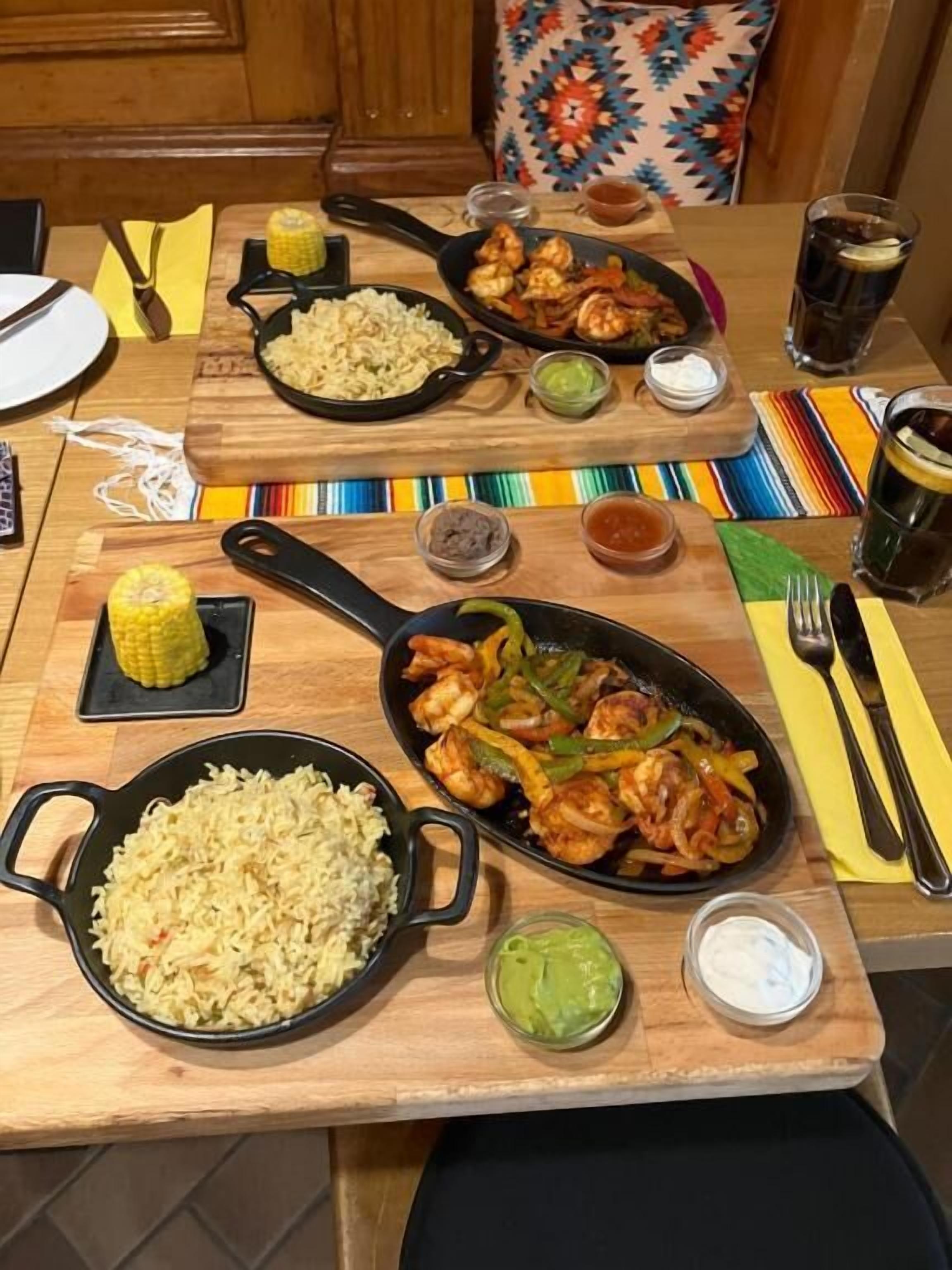 A dining table with various dishes including rice, shrimp, and vegetables, along with condiments and drinks.