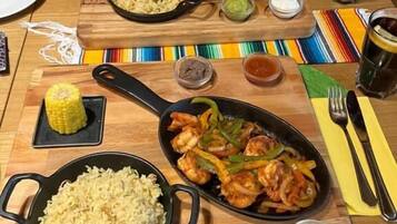 A dining table with various dishes including rice, shrimp, and vegetables, along with condiments and drinks.