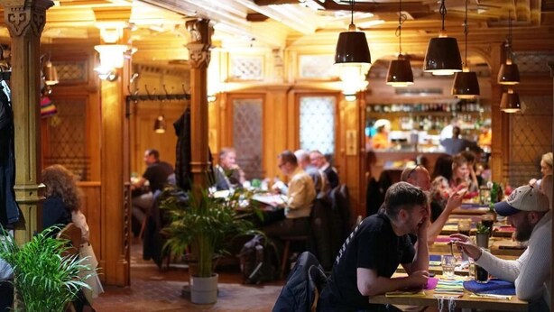 Un restaurante acogedor con interiores de madera, comensales sentados en mesas y lámparas colgantes.